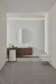 Badezimmeransicht mit modernen Elementen, inklusive einer chromfarbenen Armatur neben einem wandhängenden Bidet und einem Waschtisch mit runder Spiegelfläche. Ideal Standard Produkte sind integriert.